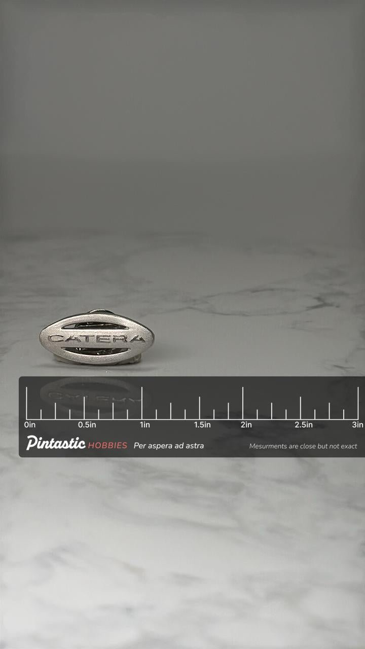 Catera Car Emblem Pin: Silver Tone Logo - 1990s Auto Accessory with ruler overlay for size reference