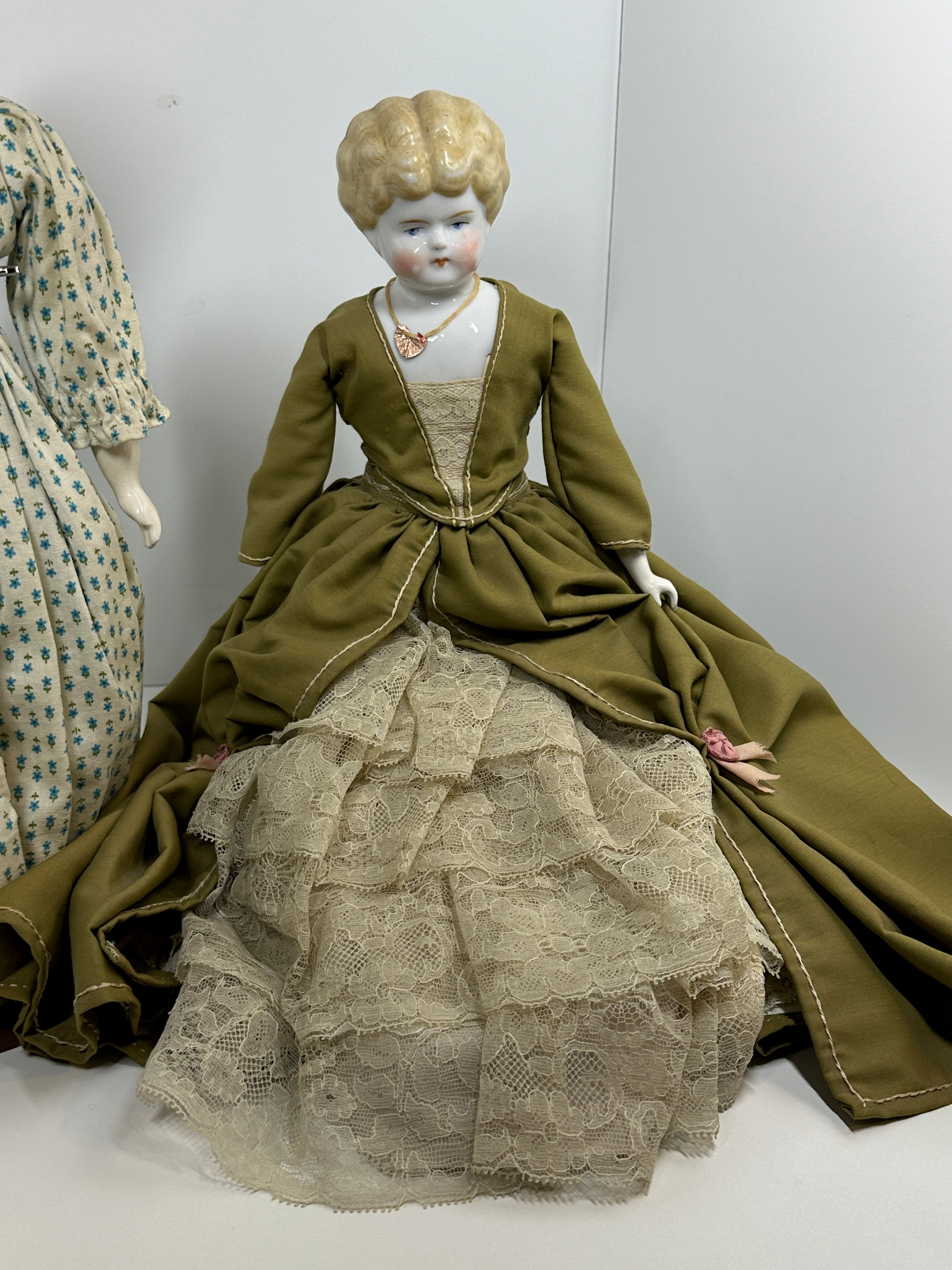 Vintage porcelain china head doll set with two dolls in period clothing, one standing and one seated with lace dress