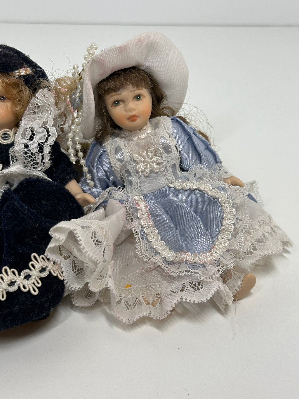 Set of two miniature porcelain dolls wearing blue vintage style lace dresses with painted faces