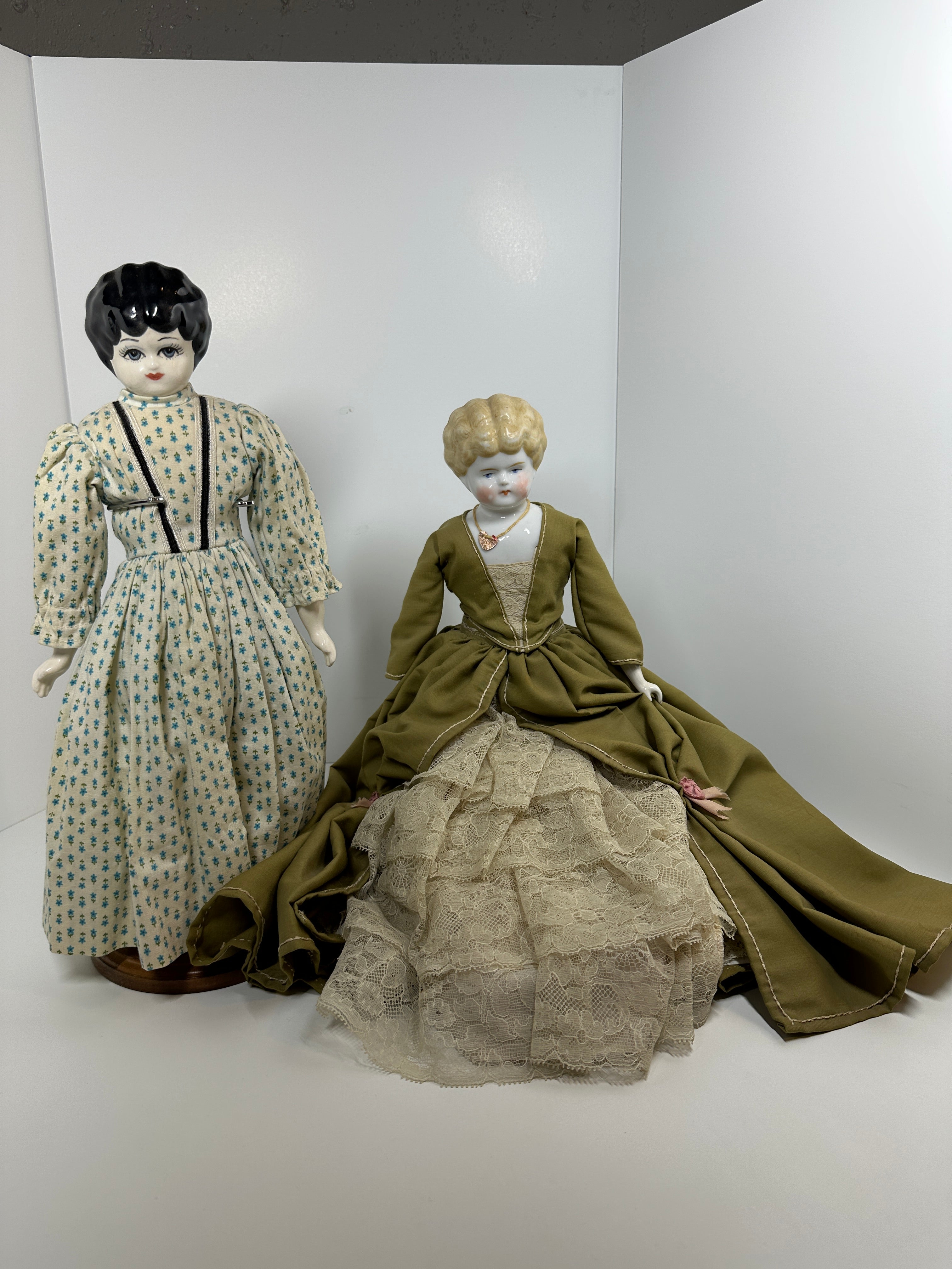 Vintage porcelain china head doll set with two dolls in period clothing, one standing and one seated with lace dress