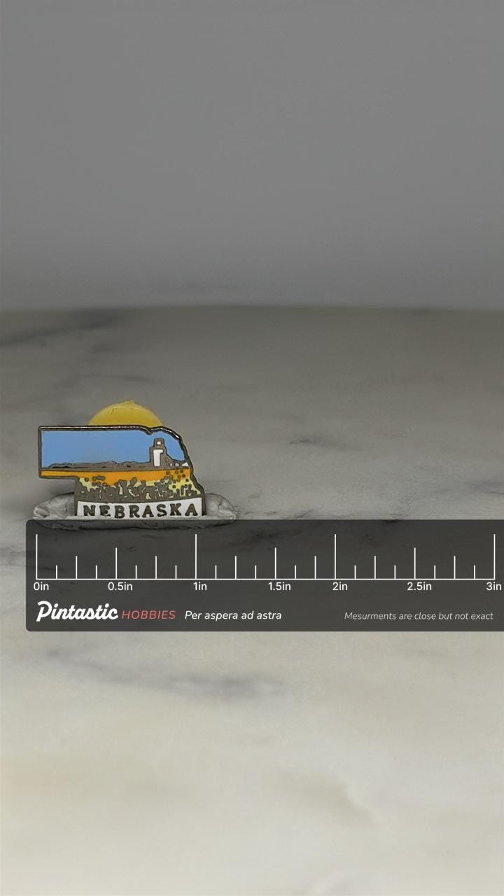 Nebraska State Enamel Pin: Blue Yellow Scenic - Vintage Travel Accessory with ruler overlay for size reference