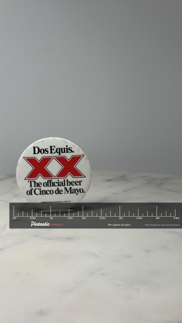 Dos Equis Beer Button Pin: Red XX Logo - 1988 Cinco de Mayo Promo with ruler overlay for size reference